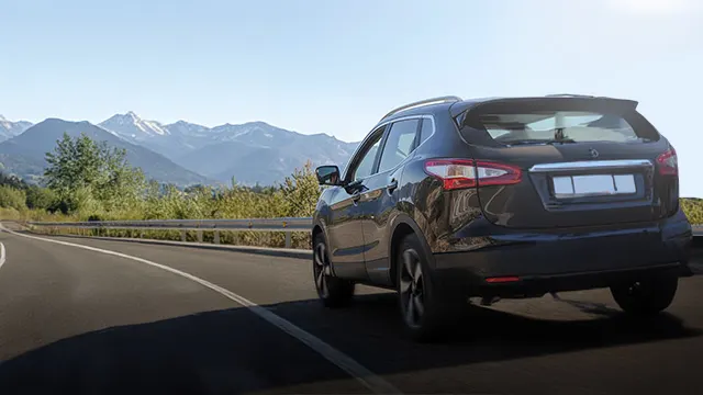 Une voiture noire est sur une route de campagne avec des montagnes au loin sous un ciel bleu clair.