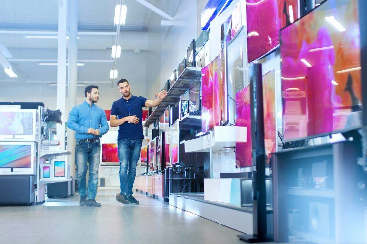 Due uomini osservano diversi televisori in un negozio di elettronica. 