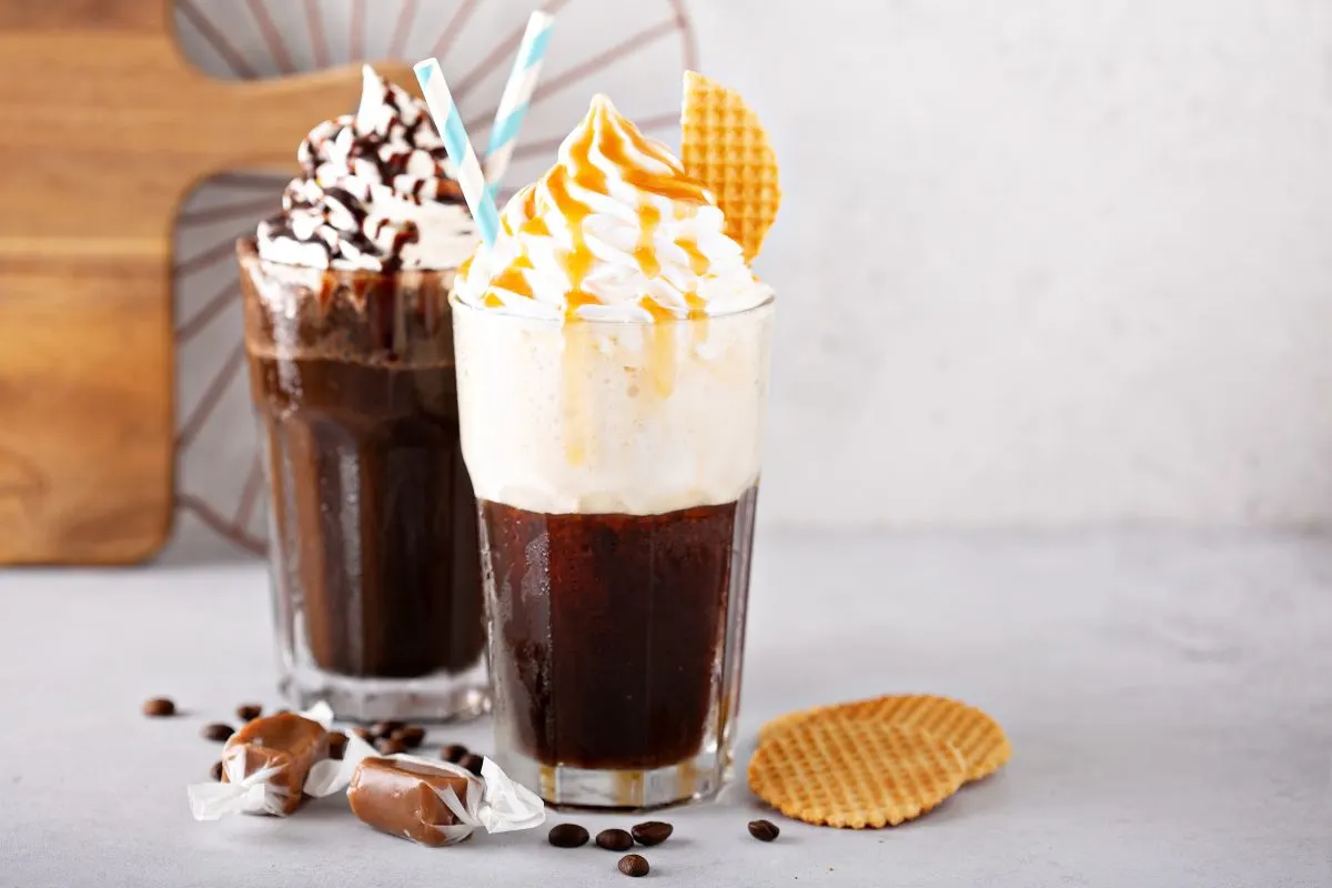 Deux cafés glacés à la crème fouettée, un caramel et gaufrette, un chocolat. Grains de café, bonbons. Fond clair, planche.