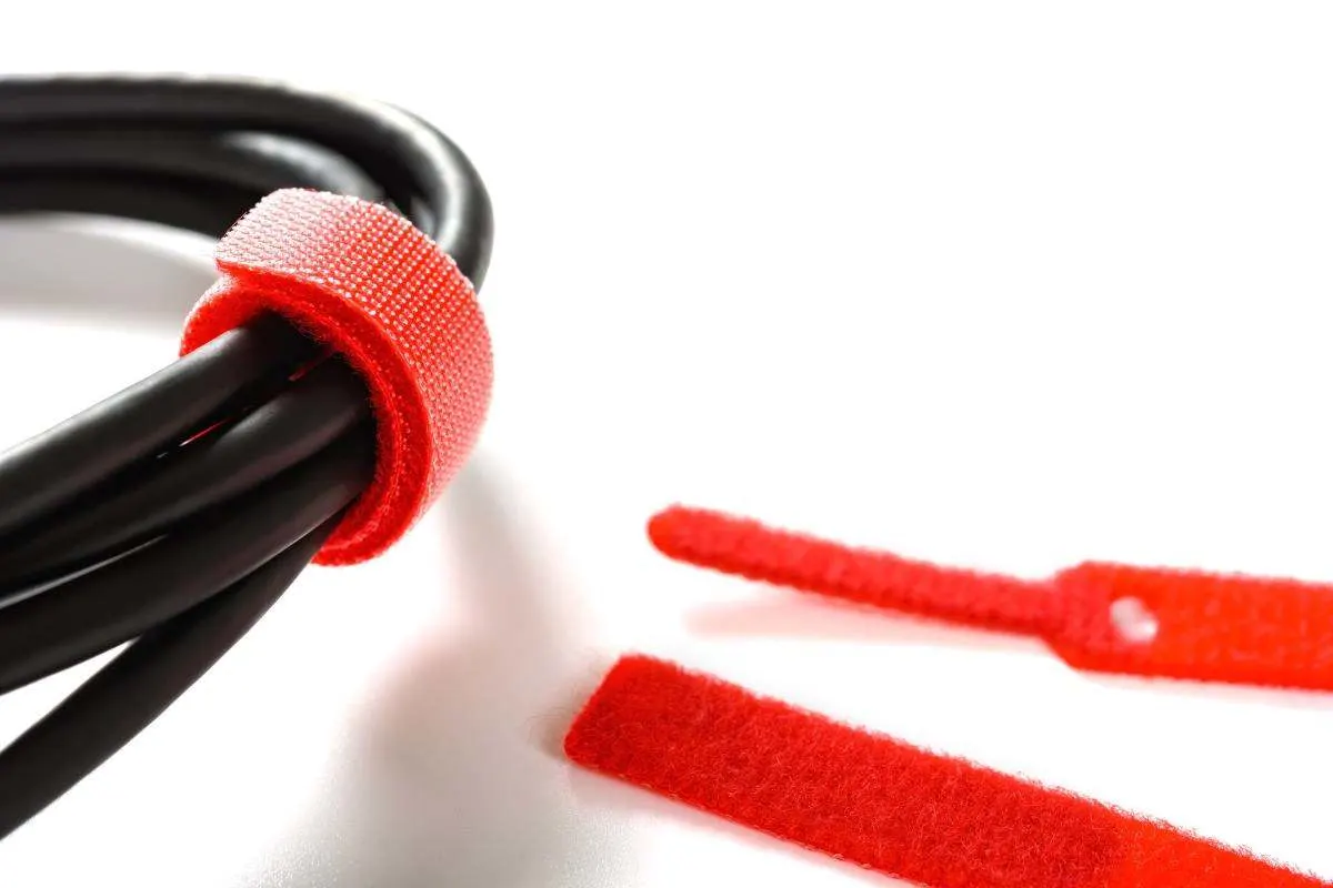 Schwarze Kabel, gebündelt mit einem roten Klettband, auf weissem Hintergrund.
