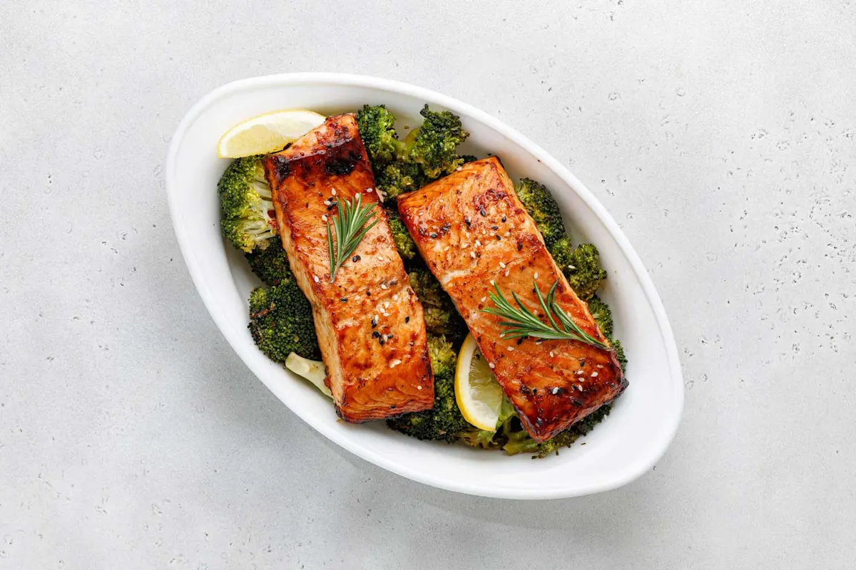 Bol contenant deux filets de saumon grillés, des bouquets de brocoli et des quartiers de citron.