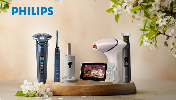 Philips-Produkte auf Holzbrett: Rasierer, Zahnbürste, Ladestation, Haarentfernungsgerät, Babyphone. Weisse Blüten im Hintergrund.