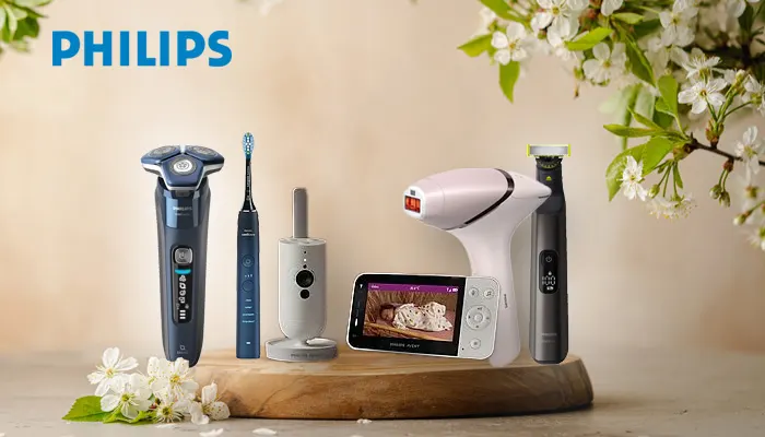 Divers appareils Philips : rasoir, brosse à dents, chargeur, épilateur et moniteur bébé sur une table en bois avec des fleurs blanches.