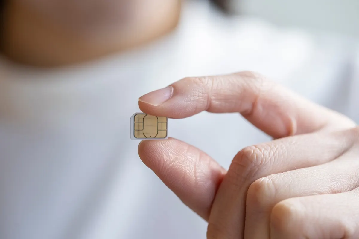 Une main tient une carte SIM entre le pouce et l’index.
