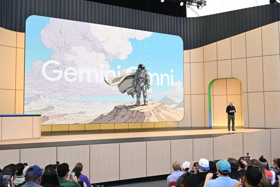 Un orateur se tient sur scène devant un écran affichant une image d’astronaute et le mot Gemini, tandis que le public prend des photos. 