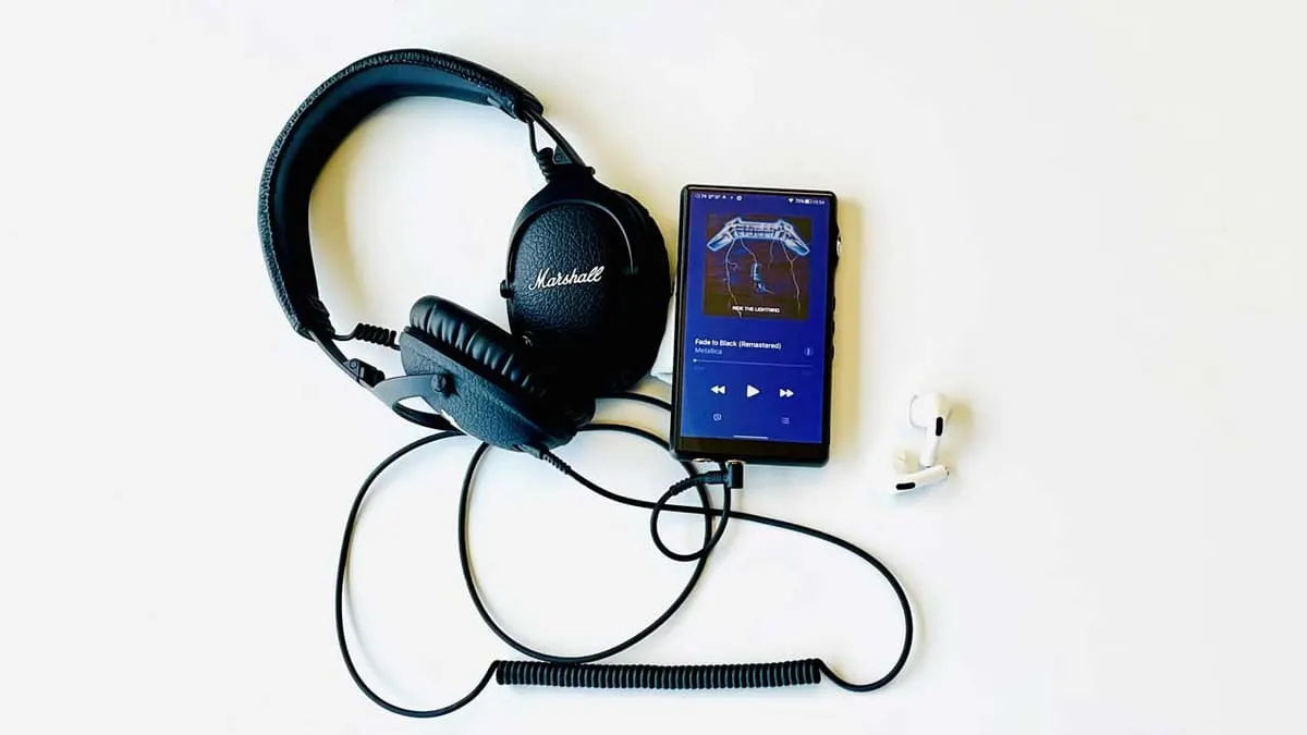 Cuffie nere Marshall, telefono con copertina album blu e auricolari bianchi su sfondo bianco.