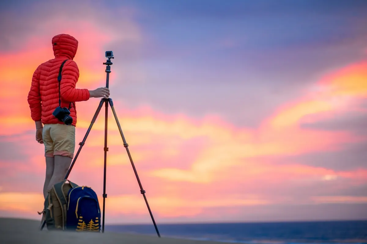 Photographe outdoor utilisant une action-cam avec trépied au coucher du soleil au bord de la mer.