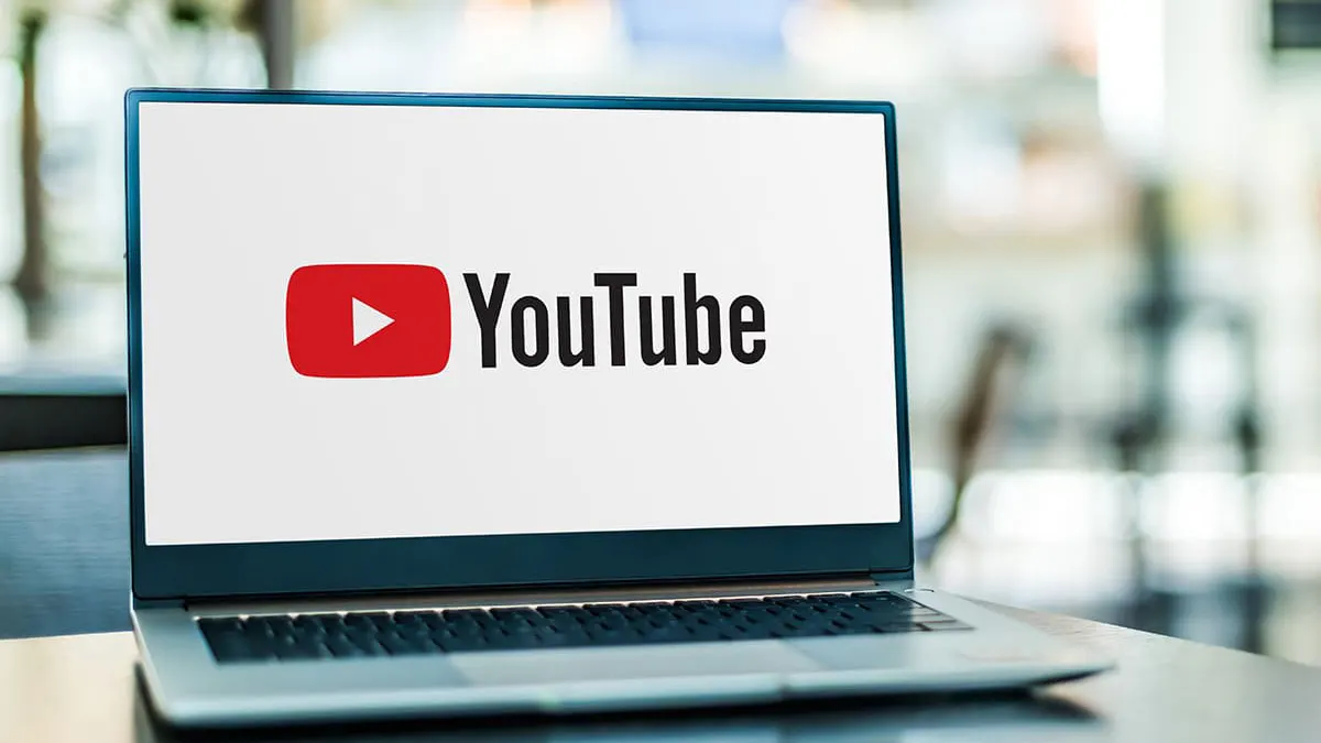 Un computer portatile mostra il logo di YouTube su uno schermo bianco. Lo sfondo è sfocato e mostra una finestra.