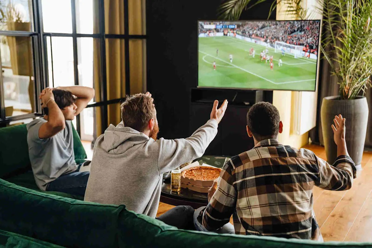 Trois hommes assis dans le salon devant la télévision, suivant un match de football.