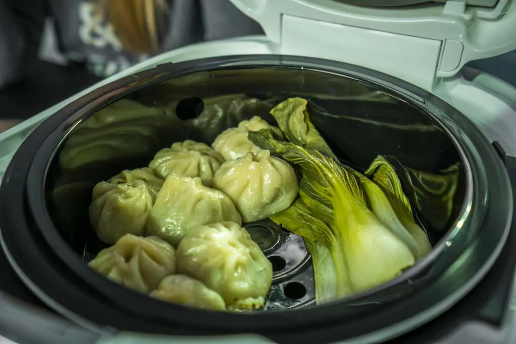 Momo al vapore e pak choi si trovano nel cestello per la cottura a vapore di un multicooker aperto. 