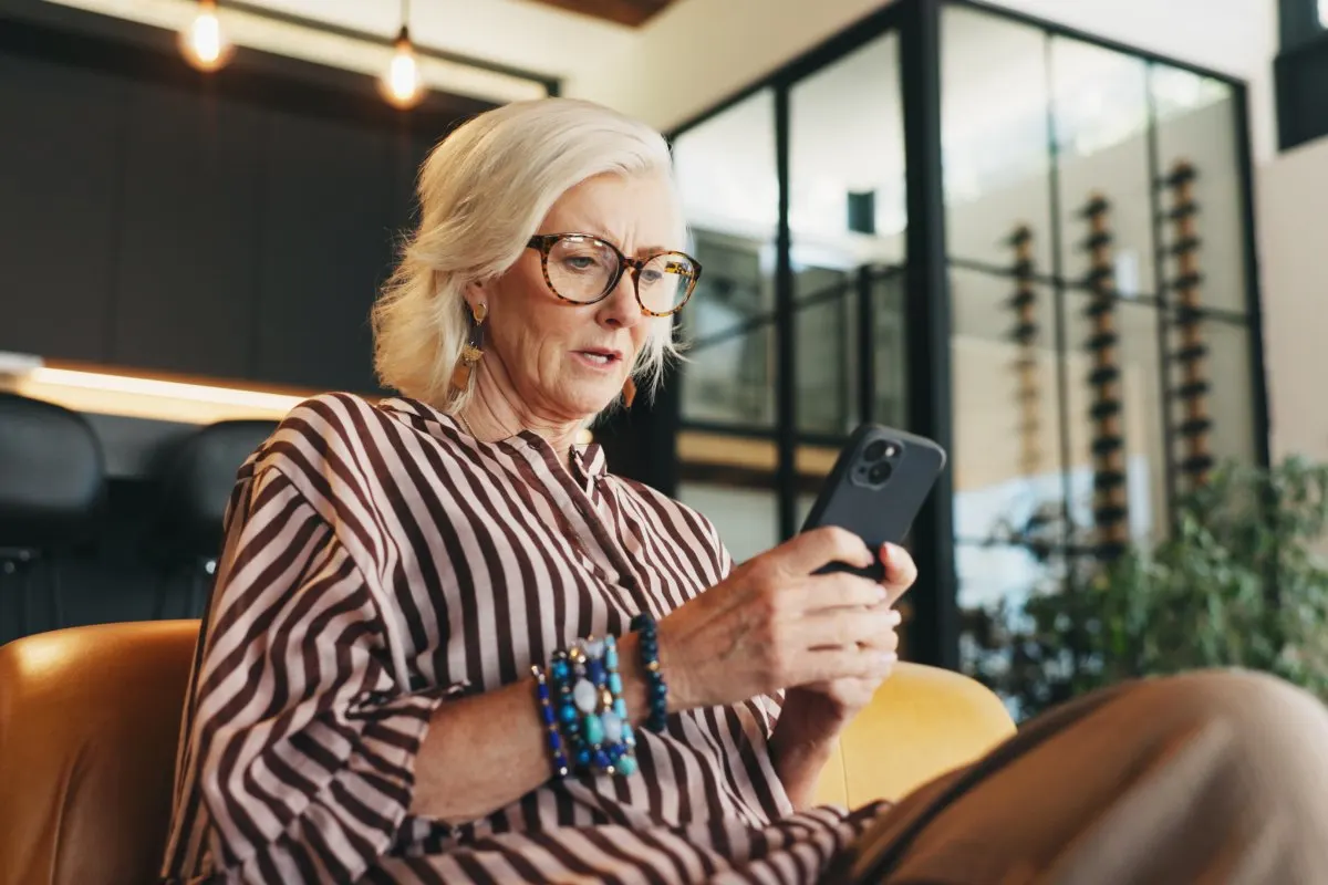 Una donna seduta su un divano guarda concentrata il suo smartphone.