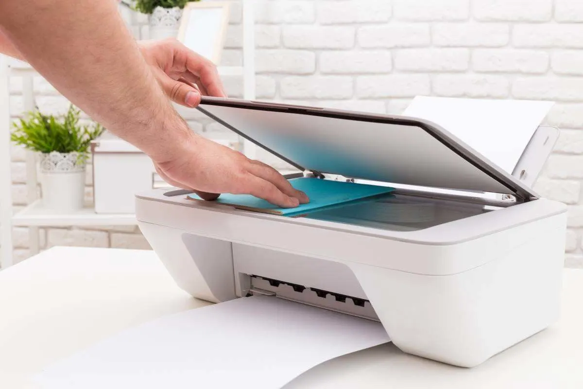 Des mains placent un document sur le scanner d’une imprimante multifonction blanche.