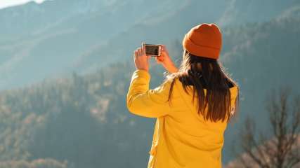 Una donna con una giacca gialla da pioggia fotografa il paesaggio con il suo smartphone.