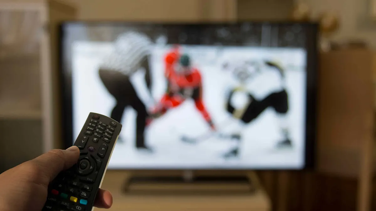 Una mano con un telecomando davanti a un televisore sul quale si vede una partita di hockey su ghiaccio.