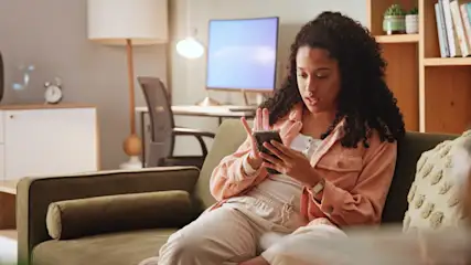 Une femme regarde son smartphone avec un air perplexe.