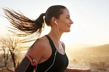 Donna che ascolta la musica mentre fa jogging con cuffie in-ear bianche.