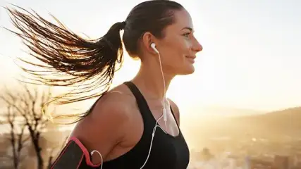 Donna che ascolta la musica mentre fa jogging con cuffie in-ear bianche.