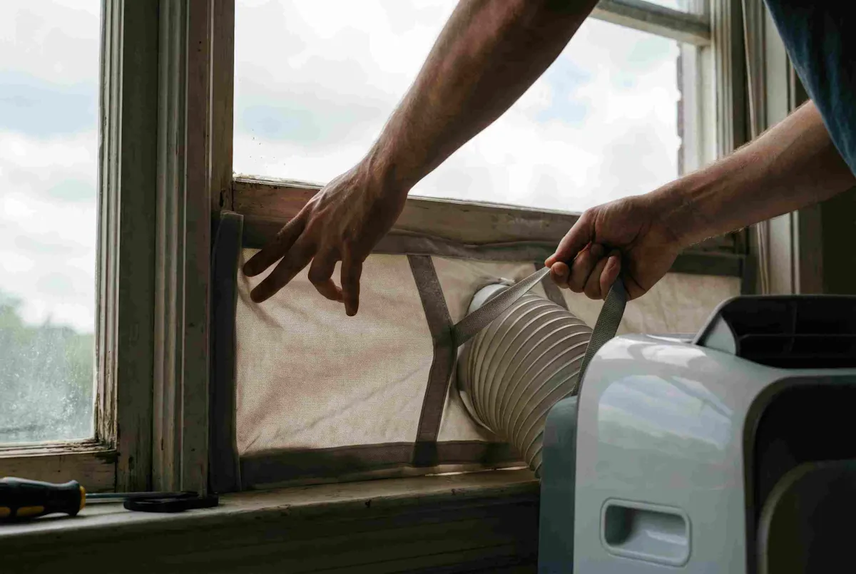 Una persona collega il tubo di scarico di un climatizzatore mobile a una finestra per espellere il calore all'esterno.