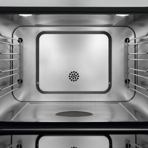 Intérieur d'un four vide en métal, avec des grilles sur les côtés et des orifices de ventilation au fond.