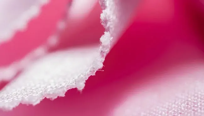 Primo piano di un tessuto rosa con bordo bianco sfrangiato, che mostra la texture e la trama del materiale.