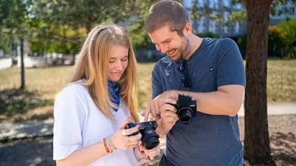 Un uomo e una donna tengono in mano una fotocamera ciascuno e controllano le impostazioni.