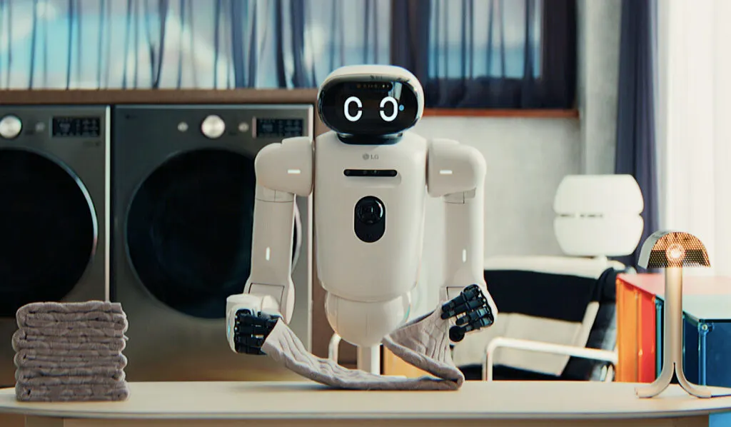 Haushaltsroboter faltet ein Küchentuch, im Hintergrund stehen zwei Waschmaschinen.