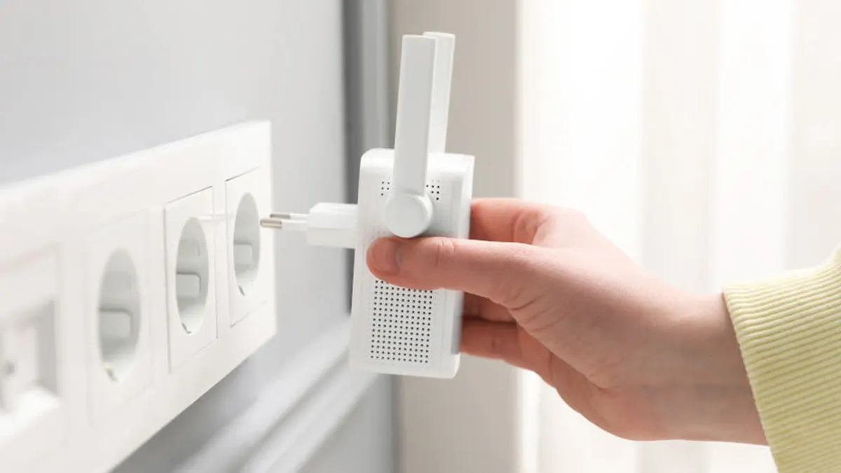 Eine Hand steckt einen weissen WLAN-Verstärker mit Antenne in eine weisse Steckdosenleiste an einer grauen Wand.