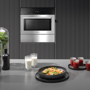 Four à  micro-ondes en acier inoxydable sur un mur à  rayures, avec un comptoir présentant des aliments et des boissons.