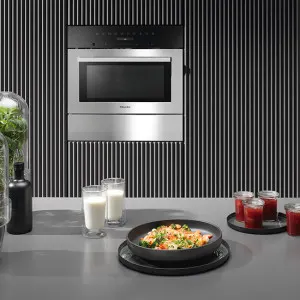 Four à micro-ondes en acier inoxydable sur un mur à rayures, avec un comptoir présentant des aliments et des boissons.