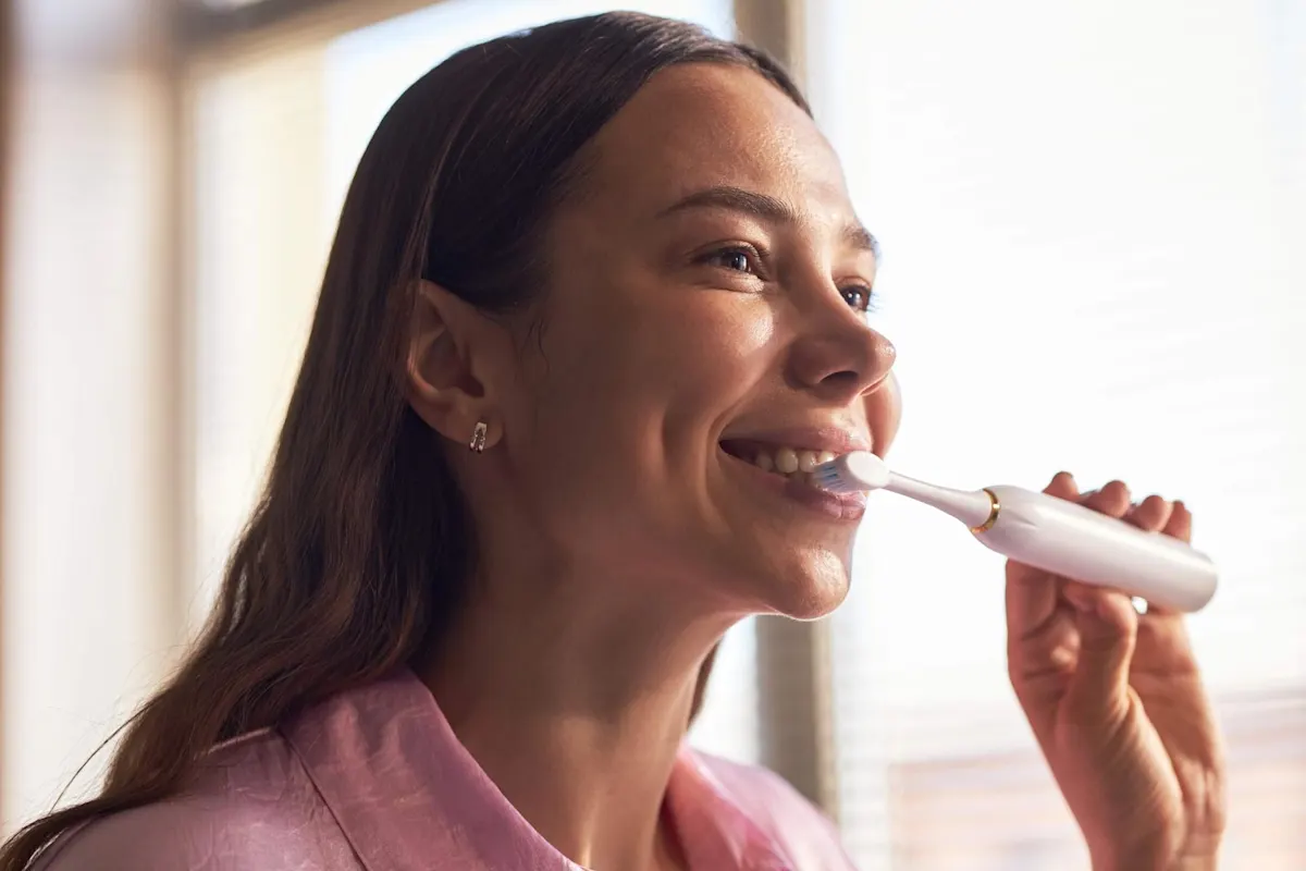 Femme aux cheveux bruns sourit en se brossant les dents.