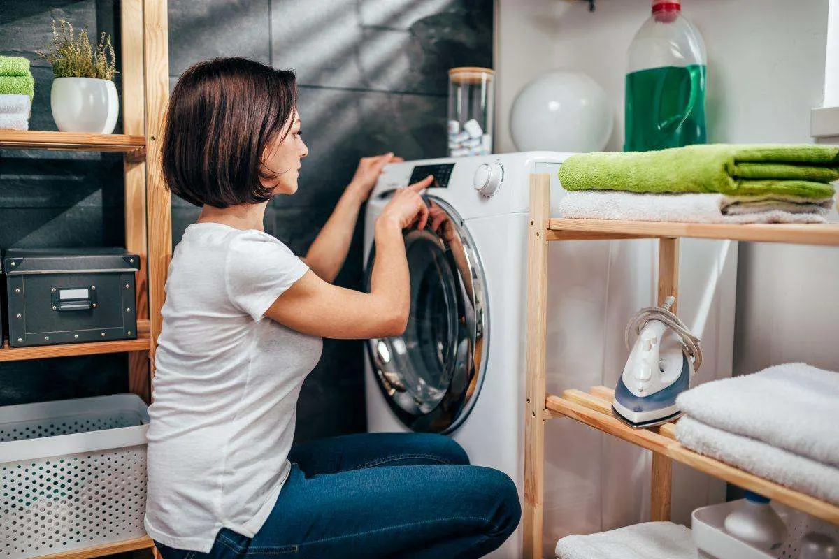 Une femme règle le programme de lavage sur une machine à laver chargée.