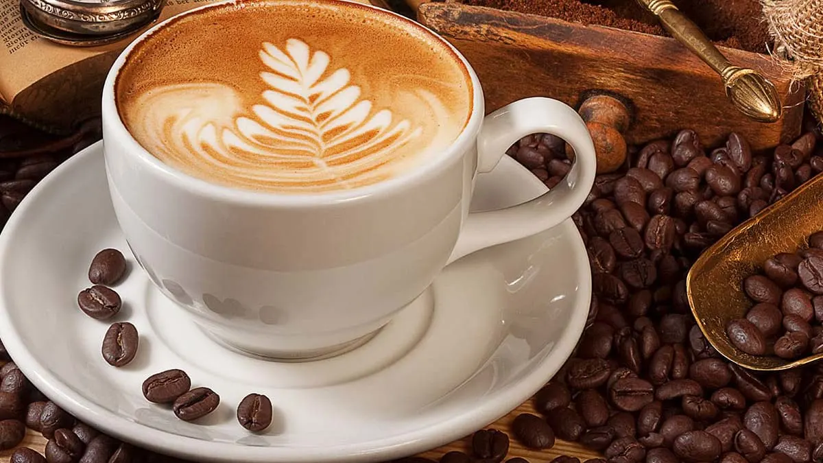 Une tasse de café avec une feuille de latte art, avec des grains de café pour décorer la soucoupe et la table.