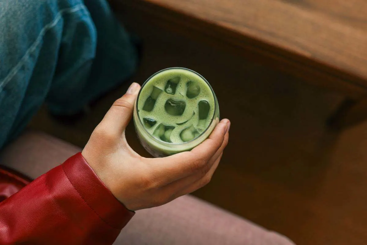 Une main tient un Iced Matcha avec des glaçons. 