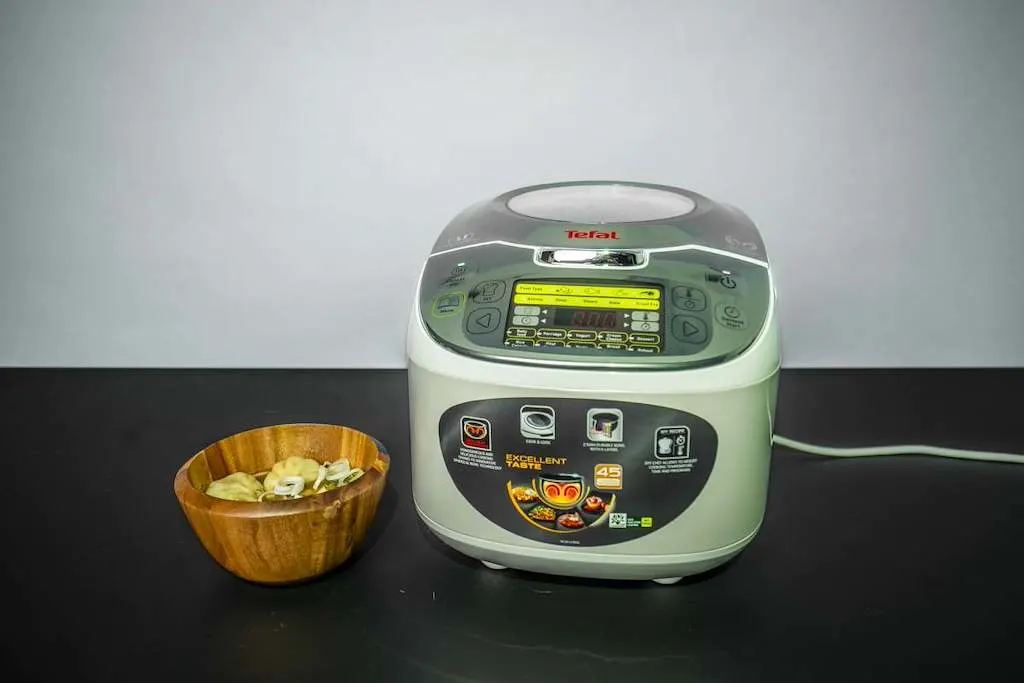 Un multicuiseur Tefal est posé sur un plan de travail à côté d’un bol en bois contenant des momos cuits à la vapeur. 