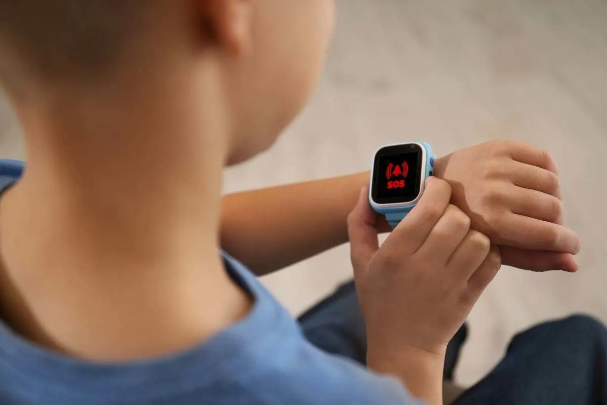 Un enfant déclenche l'appel d'urgence SOS sur une montre connectée enfant avec un écran SOS rouge