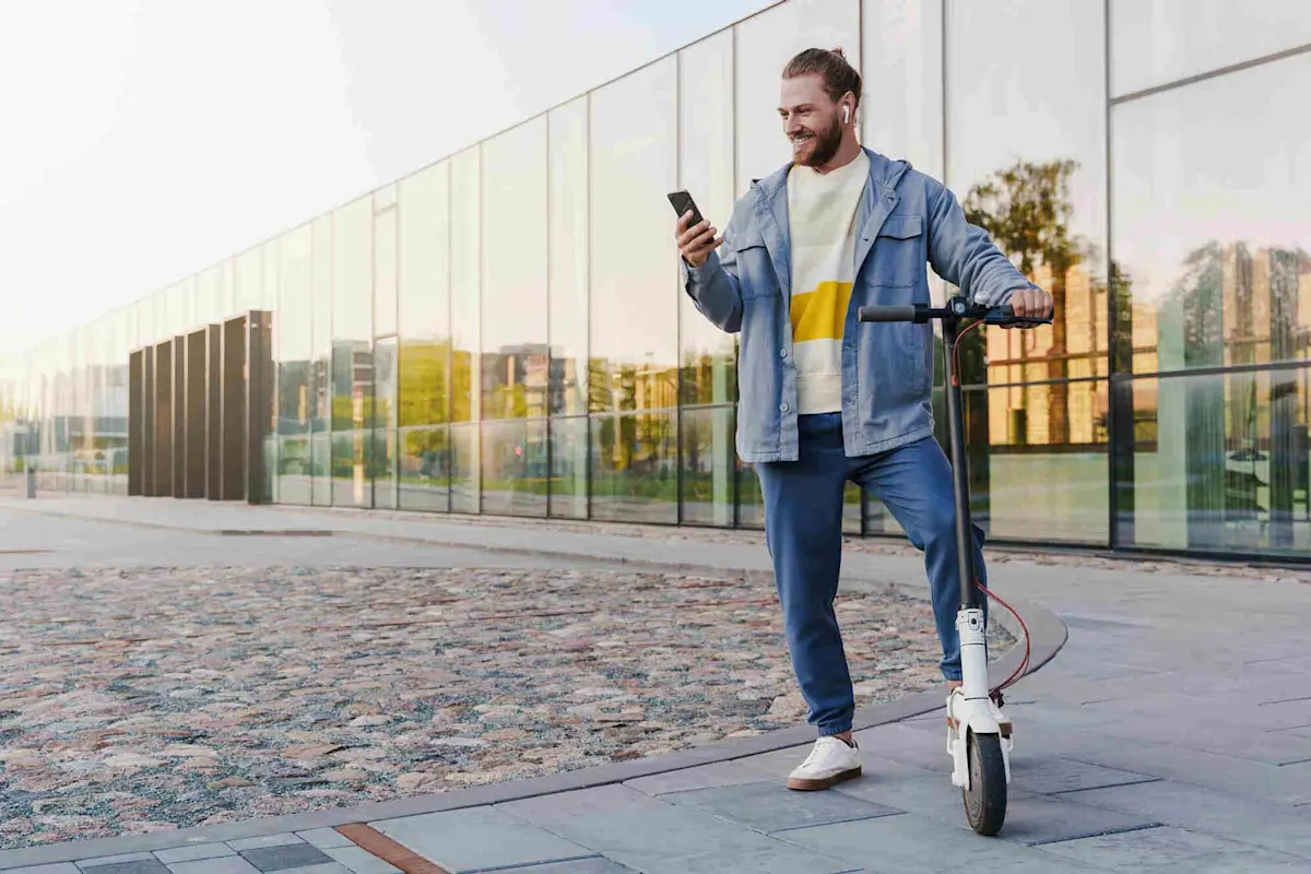 Homme tenant un e-scooter et regardant son téléphone. 