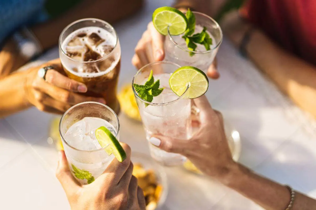 Plusieurs personnes trinquent avec des boissons fraîches, des citrons verts et de la menthe. 