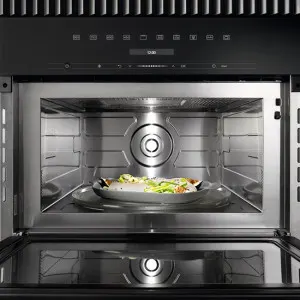 Four ouvert avec un plat rond contenant des aliments au centre, intérieur métallique avec source de lumière visible.