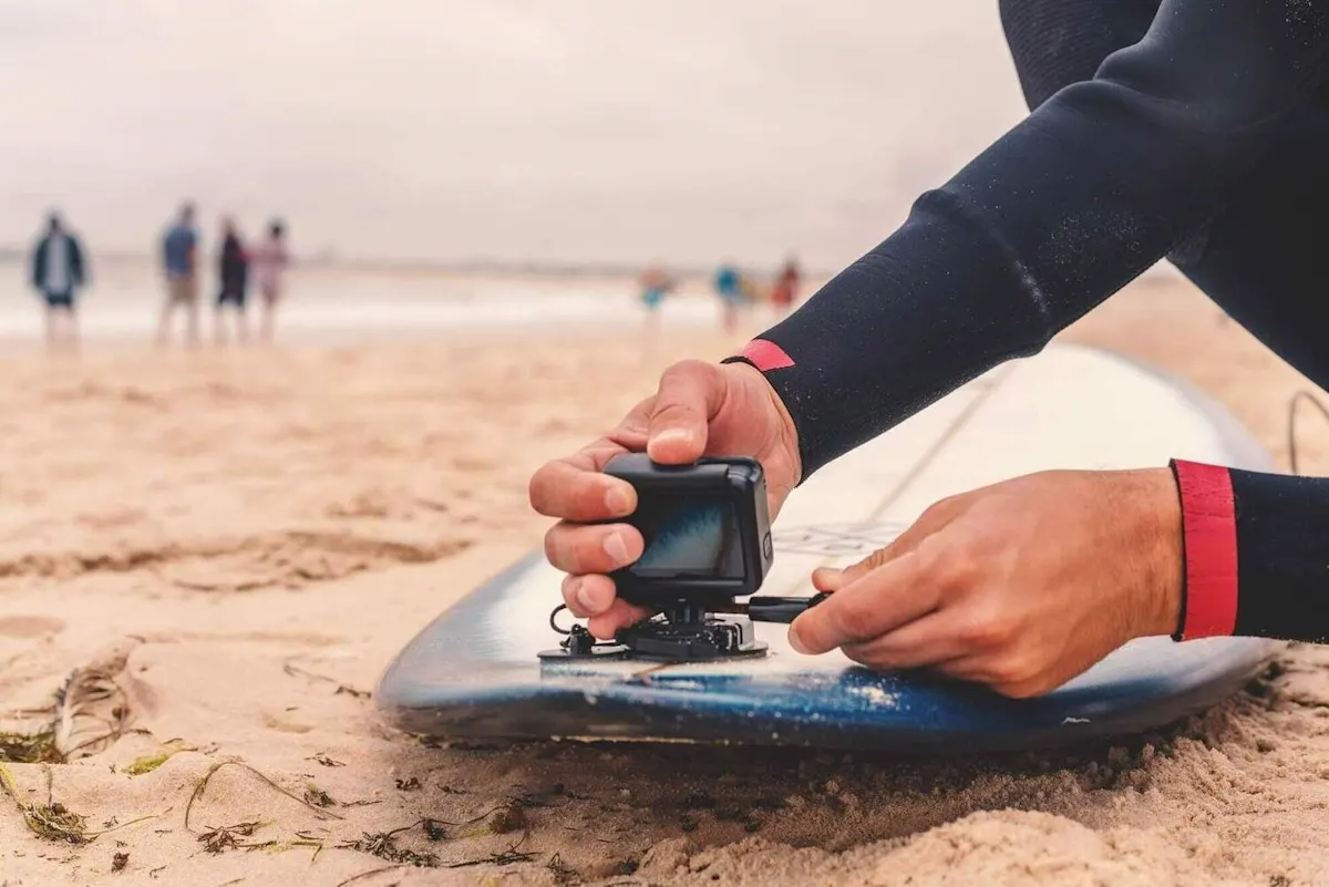 Persona che fissa una Action Cam su una tavola da surf in spiaggia.