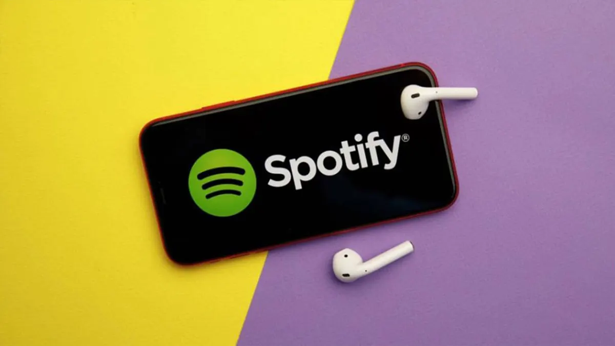Un telefono mostra il logo Spotify su sfondo nero, con auricolari bianchi su sfondo giallo e viola.