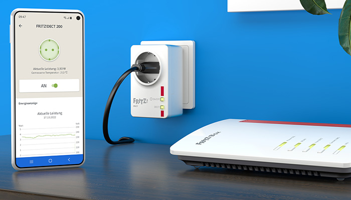 Ein Smartphone zeigt die FRITZ!DECT 200 App. Eine smarte Steckdose ist an der Wand montiert, mit einem Router im Hintergrund.
