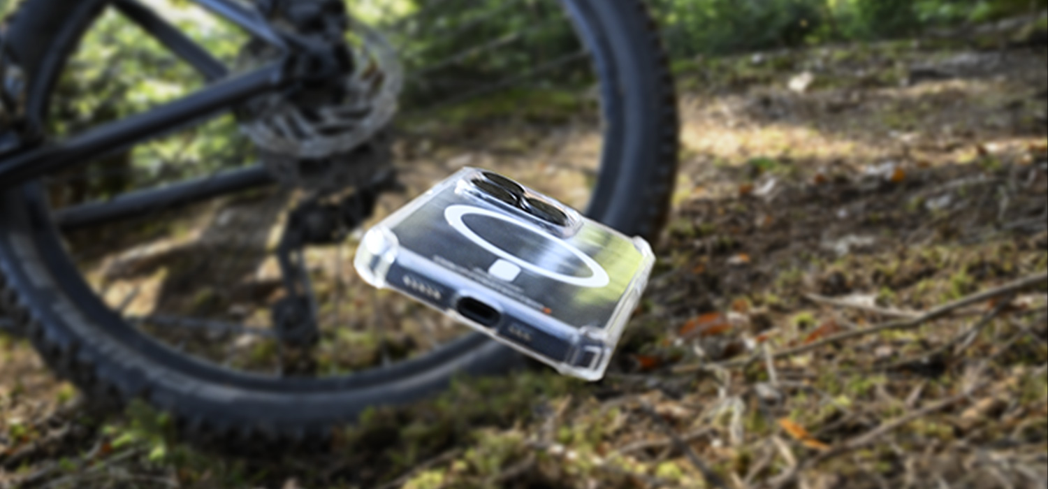 Das Hinterrad eines Mountainbikes schliddert schräg über einen Waldboden, im Vordergrund fliegt dem Betrachter eine transparente Handhülle entgegen.