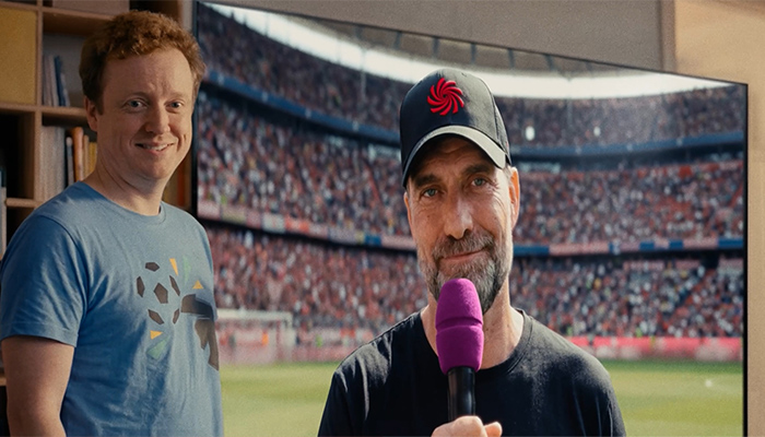 Glücklicher Konsument steht vor seinem neu gekauften Riesen-Fernseher. Darauf zu sehen: Interview mit Jürgen Klopp.