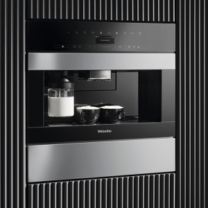 Ein schwarzer Einbaukaffeevollautomat mit silberfarbenen Akzenten und zwei Tassen, eingebaut in eine Wand mit vertikalen Streifen.