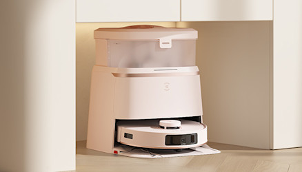 Weißer Roboterstaubsauger in Ladestation unter einem Schrank. Die Station ist weiß mit einem durchsichtigen Behälter oben.