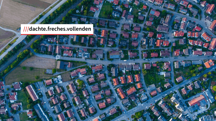 Luftaufnahme einer Wohngegend mit Häusern, Straßen und Grünflächen. Ein Feld und ein Straßenabschnitt sind ebenfalls sichtbar.