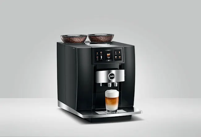 Hier ist eine Kaffeemaschine mit Bohnenbehältern oben und einem Glas Kaffee auf der Ablage.