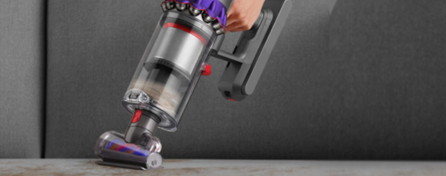 Eine Hand hält einen kabellosen Staubsauger mit durchsichtigem Behälter vor einem grauen Hintergrund.