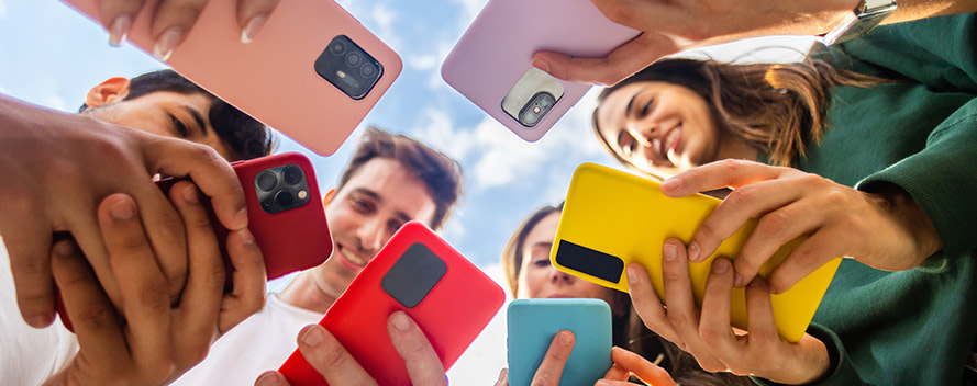 Eine Gruppe junger Erwachsener steht im Kreis und schaut auf ihre Smartphones in bunten Hüllen.