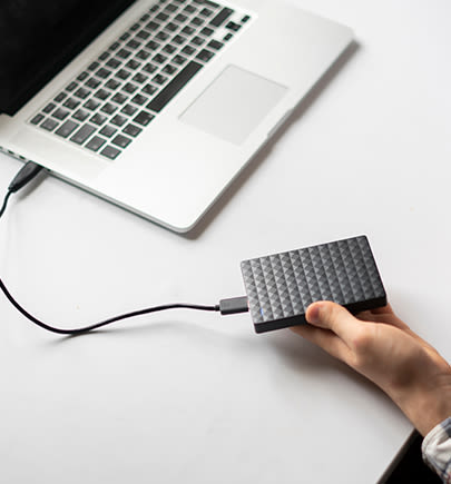 Eine Externe Festplatte, die mit einem Laptop verbunden ist, wird in der Hand gehalten